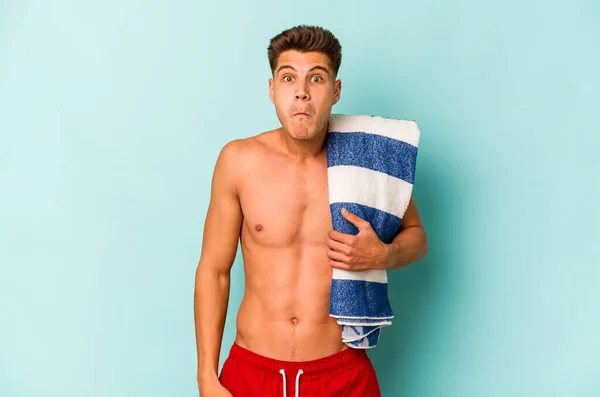 Young Caucasian Man Holding Beach Towel Isolated Blue Background Shrugs — Stock Photo, Image