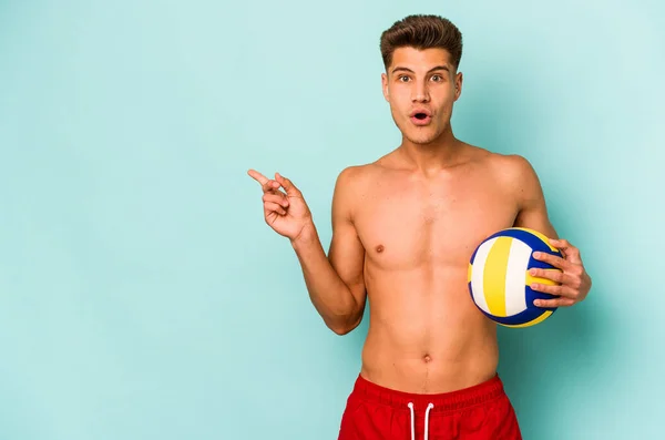 Young Caucasian Man Playing Volley Isolated Blue Background Pointing Side — Stok fotoğraf