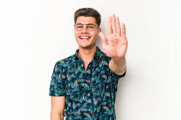 Beyaz arka planda izole edilmiş genç beyaz bir adam gülümseyerek beş numarayı parmaklarıyla gösteriyor..