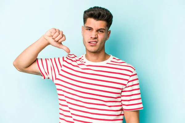 Mavi arka planda izole genç beyaz adam baş parmağını aşağı gösteriyor, hayal kırıklığı konsepti.