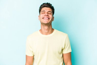 Mavi arka planda izole edilmiş genç beyaz adam gülüyor ve gözlerini kapıyor, rahatlamış ve mutlu hissediyor..