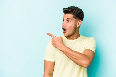 Kafkasyalı genç adam mavi arka plan noktalarında izole edilmiş başparmak uzakta, gülüyor ve kaygısız.