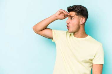 Kafkasyalı genç adam mavi arka planda izole edilmiş, uzaklara bakıyor ve elini alnına koyuyor..