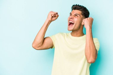 Mavi arka planda izole edilmiş genç beyaz bir adam zaferden sonra yumruğunu kaldırıyor, kazanan konsept..