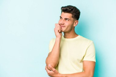 Mavi arka planda izole edilmiş genç beyaz adam rahatlamış bir şeyin fotokopi odasına baktığını düşünüyor..