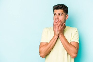 Kafkasyalı genç adam mavi arka planda izole edilmiş. Düşünceli bir şekilde ağzıyla ağzını kapatan bir fotokopi odasına bakıyor..