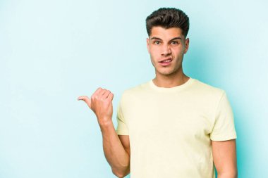 Mavi arka planda izole edilmiş genç beyaz adam işaret parmağıyla fotokopi alanını işaret ederek şok oldu..