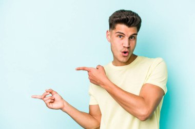 Mavi arka planda izole edilmiş genç beyaz adam işaret parmağıyla fotokopi alanını işaret ederek heyecan ve arzusunu ifade ediyor..