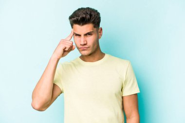 Mavi arka planda izole edilmiş genç beyaz bir adam şakağı parmağıyla işaret ediyor, düşünüyor ve bir göreve odaklanıyor..