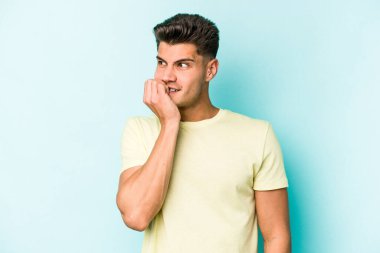 Mavi arka planda izole edilmiş, tırnak yiyen, gergin ve endişeli genç bir beyaz adam..