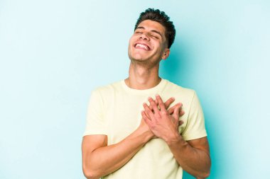 Mavi arka planda izole edilmiş beyaz bir genç, dost bir ifadeye sahip, avuçlarını göğsüne bastırıyor. Aşk konsepti.