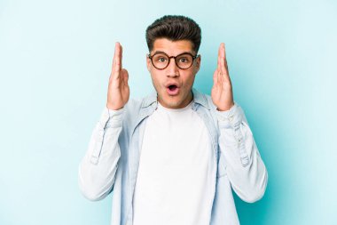 Kafkasyalı genç adam mavi arka planda izole edildi. Şaşırdı ve şok oldu..