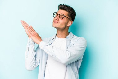 Kafkasyalı genç adam mavi arka planda izole edilmiş enerjik ve rahat hissediyor, ellerini ovuşturuyor kendinden emin.