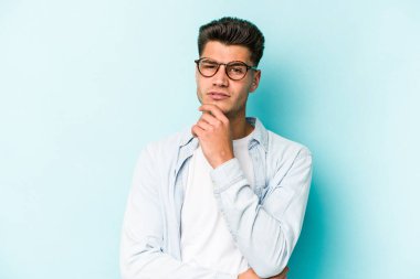 Kafkasyalı genç adam mavi arka planda izole edilmiş şüpheli, belirsiz, seni muayene ediyor..