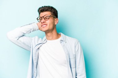 Kafkasyalı genç adam mavi arka planda izole edilmiş. Yorgun ve uykulu. Elini başının üstünde tutuyor..