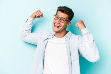 Kafkasyalı genç adam mavi arka planda izole edilmiş kaygısız ve heyecanlı tezahüratlar yapıyor. Zafer konsepti.