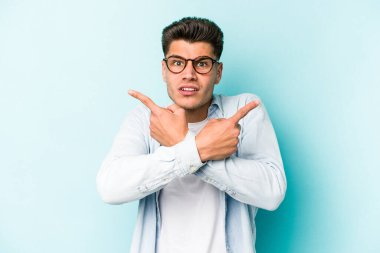 Mavi arka plan noktalarında izole genç beyaz adam, iki seçenek arasında seçim yapmaya çalışıyor.