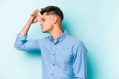 Kafkasyalı genç bir adam mavi arka planda izole edilmiş, başı ağrıyor, yüzüne dokunuyor..