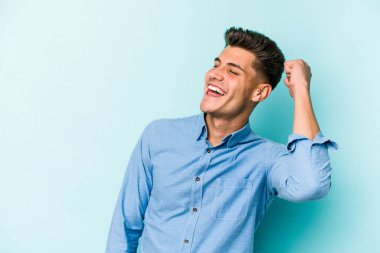 Mavi arka planda izole edilmiş genç beyaz bir adam zaferi, tutkuyu ve coşkuyu kutluyor, mutlu bir ifade..