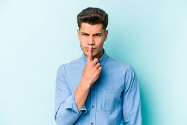 Kafkasyalı genç adam mavi arka planda izole edilmiş düşünüyor ve bakıyor, yansıtıyor, düşünüyor, bir fantezi kuruyor..