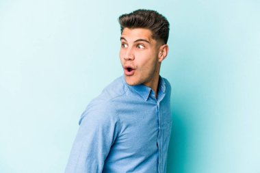 Mavi arka planda soyutlanmış genç beyaz bir adam gülümsüyor, neşeli ve keyifli görünüyor..
