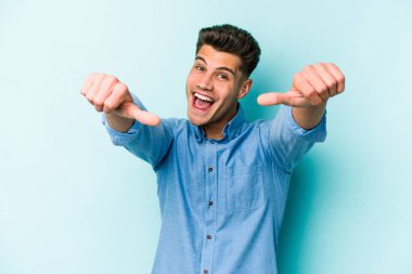 Kafkasyalı genç adam mavi arka planda izole edilmiş. Baş parmağını kaldırıyor, gülümsüyor ve kendinden emin..