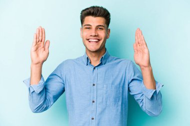 Kafkasyalı genç adam mavi arka planda izole edilmiş. Elinde işaret parmaklarıyla küçük bir şey tutuyor, gülümsüyor ve kendinden emin..