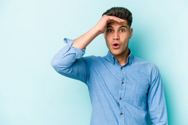 Kafkasyalı genç adam mavi arka planda izole edilmiş, uzaklara bakıyor ve elini alnına koyuyor..