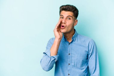 Mavi arka planda izole edilmiş genç beyaz bir adam gizli bir sıcak fren haberi veriyor ve yana bakıyor.