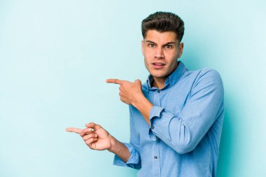 Mavi arka planda izole edilmiş genç beyaz adam işaret parmağıyla fotokopi alanını işaret ederek şok oldu..