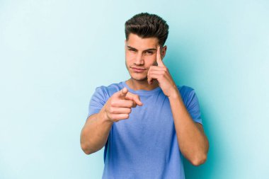 Mavi arka planda izole edilmiş genç beyaz bir adam şakağı parmağıyla işaret ediyor, düşünüyor ve bir göreve odaklanıyor..