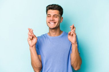 Kafkasyalı genç adam mavi arka planda izole edilmiş şans dilemek için şans diliyor.