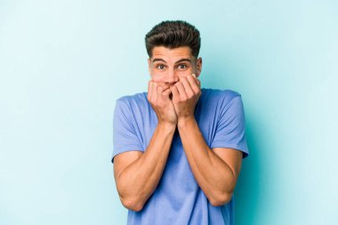 Mavi arka planda izole edilmiş, tırnak yiyen, gergin ve endişeli genç bir beyaz adam..