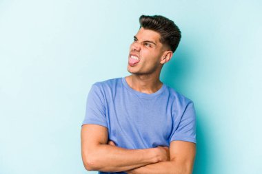 Kafkasyalı genç adam mavi arka planda izole edilmiş komik ve dost canlısı bir dil uzatıyor..