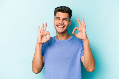 Kafkasyalı genç adam mavi arka planda izole edilmiş neşeli ve kendinden emin..