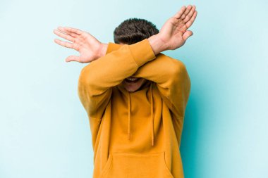 Kafkasyalı genç adam mavi arka planda izole edilmiş iki kolu çapraz tutuyor, inkar kavramı.