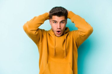 Genç beyaz adam mavi arka planda izole edilmiş bağırıyor, çok heyecanlı, tutkulu, bir şeyden memnun..