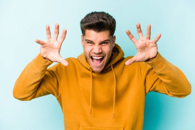 Mavi arka planda izole edilmiş genç beyaz adam pençelerini kedi taklidi yaparken gösteriyor, agresif bir hareket..