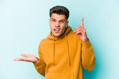 Kafkasyalı genç adam mavi arka planda izole edilmiş ve elinde bir ürün tutuyor..