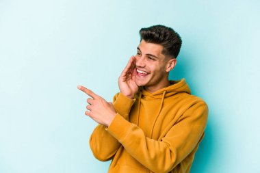 Kafkasyalı genç adam mavi arka planda izole edilmiş. Dedikodu yapıyor, bir şeyleri bildiriyor..