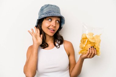 Beyaz arka planda izole edilmiş bir çanta dolusu cipsi tutan genç İspanyol kadın bir dedikoduyu dinlemeye çalışıyor..