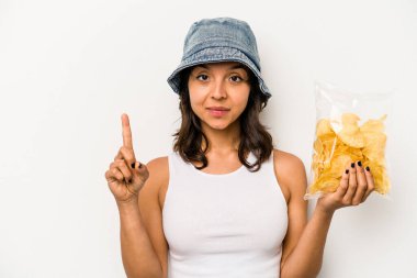 Beyaz arka planda izole edilmiş bir paket cipsi tutan genç İspanyol kadın bir numarayı parmağıyla gösteriyor..