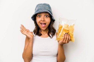 Beyaz arka planda izole edilmiş bir paket cipsi tutan genç İspanyol kadın şaşırdı ve şok oldu..