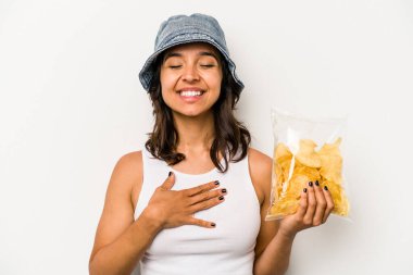 Beyaz arka planda izole edilmiş bir paket cipsi tutan genç İspanyol kadın kahkahalarla gülüyor..