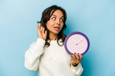 Mavi arka planda bir saat tutan genç İspanyol kadın bir dedikoduyu dinlemeye çalışıyor..