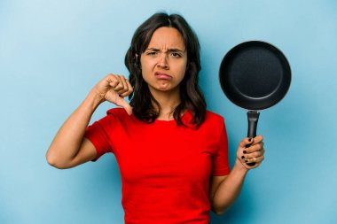 Mavi arka planda izole edilmiş bir tava tutan genç İspanyol kadın hoşlanmadığı bir jest gösteriyor. Anlaşmazlık konsepti.