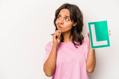 Beyaz arka planda izole edilmiş, şüpheli ve şüpheci bir ifadeyle yan bakan acemi sürücü tabelasını tutan genç İspanyol kadın..