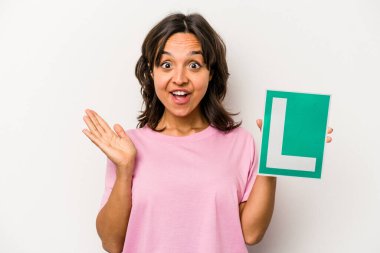 Genç bir İspanyol kadının elinde acemi sürücü tabelası var. Beyaz arka planda izole edilmiş. Şaşırmış ve şok olmuş..