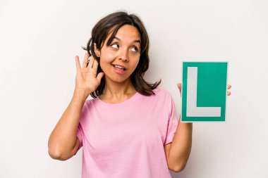 Beyaz arka planda izole edilmiş acemi sürücü tabelasını tutan genç İspanyol kadın bir dedikoduyu dinlemeye çalışıyor..