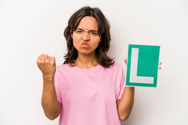 Genç İspanyol kadın elinde acemi sürücü tabelası var. Beyaz arka planda izole edilmiş. Kameraya yumruk, agresif yüz ifadesi gösteriyor..